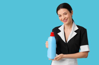 Mavi arka planda bir şişe deterjanı olan güzel bir oda hizmetçisi.