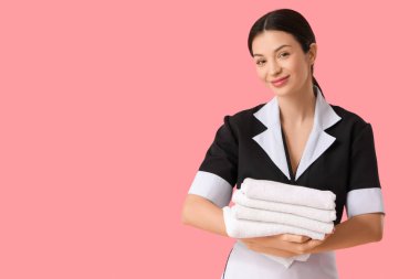 Pembe arka planda bir yığın temiz havlusu olan güzel bir oda hizmetçisi.