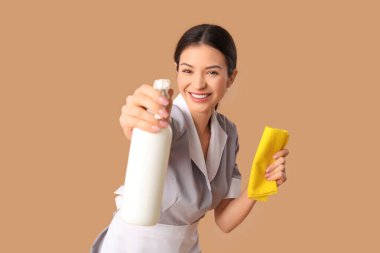 Bej arka planda bir şişe deterjanı ve paçavrası olan güzel bir oda hizmetçisi.