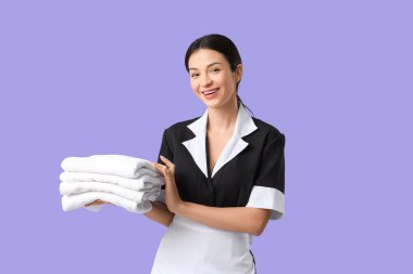 Mor arka planda bir yığın temiz havlusu olan güzel bir oda hizmetçisi.