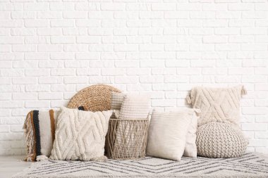 Halıda dekoratif yastıklar olan sepet beyaz tuğla duvarın yanında.