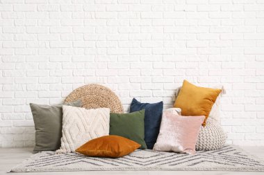 Dekoratif yastıklar halının üzerinde puflarla beyaz tuğla duvarın yanında, odada.