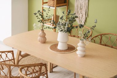 Yemek masasındaki vazolarda okaliptüs dalları. Odadaki yeşil duvarın yanında.