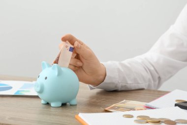 İş kadını masadaki domuz kumbarasına para yatırıyor arka planda ışığa karşı, yakın plan. Mali Sağlık Ayı