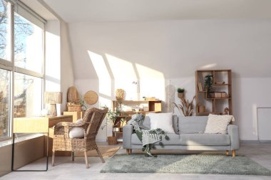 Büyük pencerenin yanında gri kanepesi ve çalışma alanı olan şık bir oturma odası.