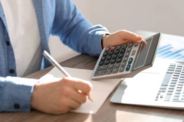 Erkek muhasebeci bir şeyler yazıyor ve ofiste hesaplamalar yapıyor. Yakın çekim.