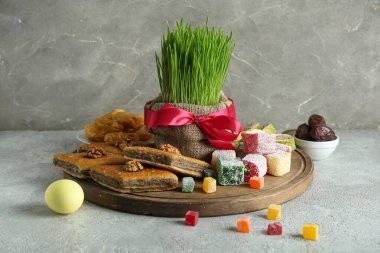 Gri grunge masasında yeşil buğday çimi, geleneksel baklava ve Türk lokumu olan bir pano. Nowruz Bayram kutlaması