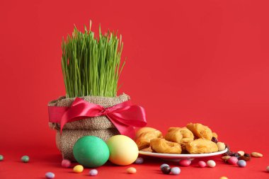 Lezzetli baklavalı yeşil buğday otları, yumurtalar ve kırmızı zemin üzerinde renkli şekerler. Nowruz Bayram kutlaması