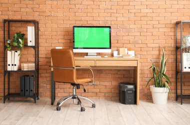 Odasında tuğla duvarın yanında bilgisayar olan modern işyeri
