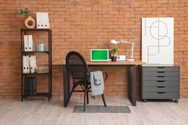 Odasında tuğla duvarın yanında dizüstü bilgisayarı olan modern işyeri