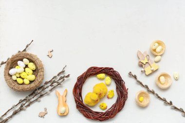 Nests with Easter eggs, wooden bunnies, chicks and pussy willow branches on white background