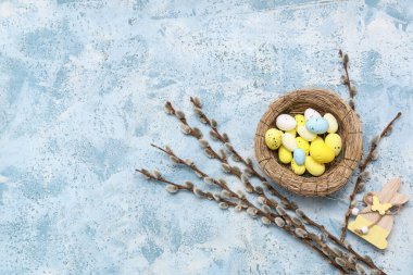 Nest with Easter eggs, wooden bunny and pussy willow branches on light blue background
