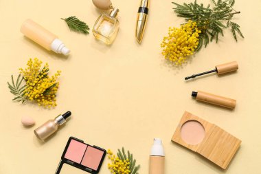 Dekoratif kozmetikten yapılmış çerçeve, sarı arka planda parfüm ve mimoza çiçekleri.