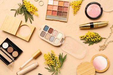 Süslü mücevherleri ve bej arka planda mimoza çiçekleri olan dekoratif kozmetikler.