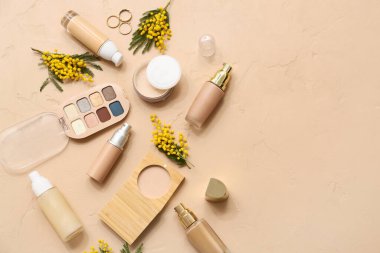 Süslü yüzüklerle dekoratif kozmetik ürünleri ve bej arka planda mimoza çiçekleri.