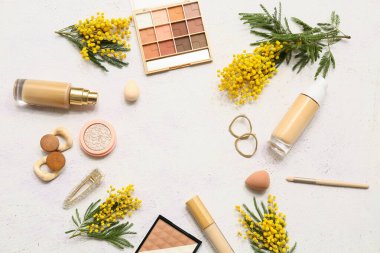 Dekoratif kozmetikten yapılmış çerçeveler şık küpeler, saç tokası ve beyaz arka planda mimoza çiçekleri.