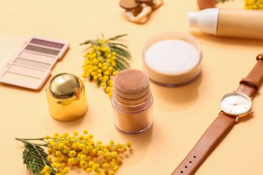 Kol saatli dekoratif kozmetik ürünler ve turuncu arka planda mimoza çiçekleri, yakın plan.