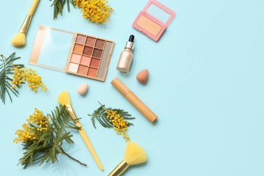 Makyaj fırçaları ve mavi arka planda mimoza çiçekleri olan dekoratif kozmetik ürünler.