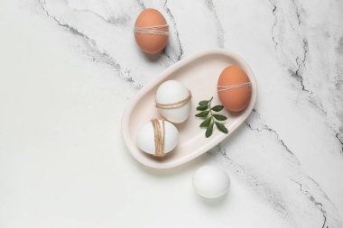 Beyaz tepsi, Paskalya yumurtası ve mermer arka planda yeşil yaprak kompozisyonu