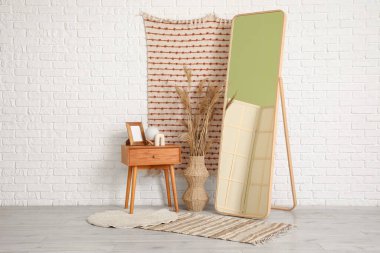 Masa, vazo, çayır otları ve odanın içindeki beyaz tuğla duvarın yanında yer aynası.