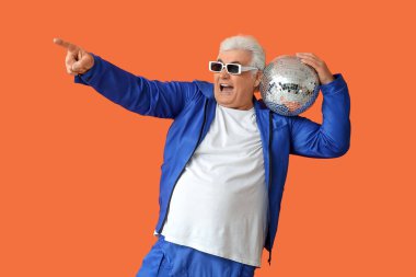 Güneş gözlüklü ve disko topuyla turuncu arka plandaki bir şeyi gösteren şık, yaşlı bir adam. Ulusal Büyükbaba Günü