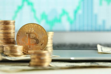 Bilgisayarın ekranının yanındaki tabloda grafikli birçok altın bitcoin var