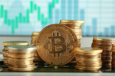 Bilgisayarın ekranının yanındaki tabloda grafikli birçok altın bitcoin var