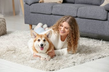 Evde yerde yatan sevimli Corgi köpeği olan genç bir kadın.