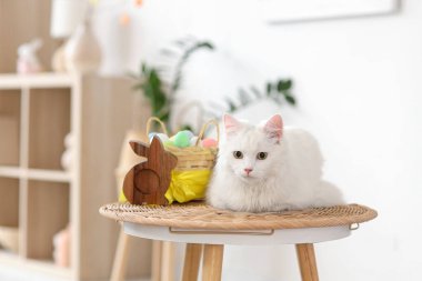 Paskalya sepeti ve evde masada oturan tahta tavşanlı şirin beyaz kedi.