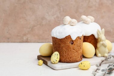 Sweet Easter cakes with yellow eggs, toy rabbit and pussy willow branches on white table
