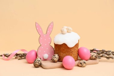 Wooden board with sweet Easter cake, eggs, toy rabbit and pussy willow branches on yellow background