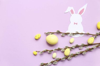 Easter eggs with paper bunny and pussy willow branches on lilac background