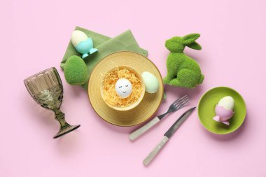 Paskalya kutlaması için şık bir masa, boyalı yumurtalar ve pembe arka planda dekoratif bir tavşan.