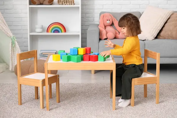 Oturma odasındaki masada plastik küpleri olan sevimli küçük kız.