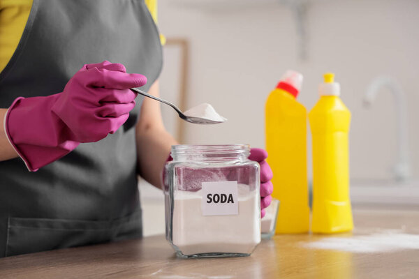 Young woman taking spoon of baking soda from jar for cleaning in kitchen, closeup