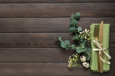 Paskalya yumurtaları, okaliptüs dalları ve ahşap arka planda çiçeklerle Paskalya kutlaması için şık bir masa.