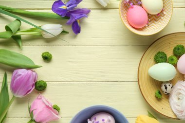 Farklı çiçeklerden yapılmış çerçeveler ve sarı ahşap arka planda Paskalya kutlaması için boyanmış yumurtalar.