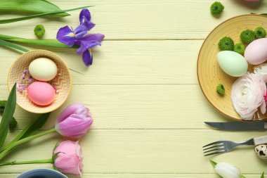 Farklı çiçeklerden yapılmış çerçeveler ve sarı ahşap arka planda Paskalya kutlaması için boyanmış yumurtalar.