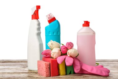 Masanın üzerinde beyaz arka planda sünger ve lale çiçekleri olan deterjan şişeleri.