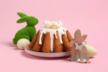 Pembe arka planda yumurta ve oyuncak tavşanlı bir tabak tatlı Paskalya ekmeği.