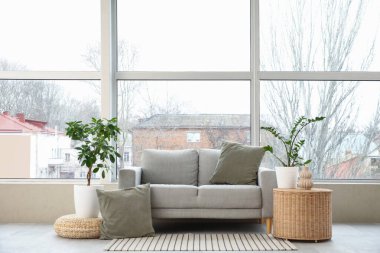 Oturma odasındaki pencerenin yanındaki rahat gri kanepe.