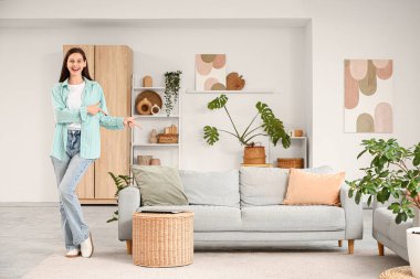 Oturma odasındaki kanepeyi gösteren mutlu genç kadın.