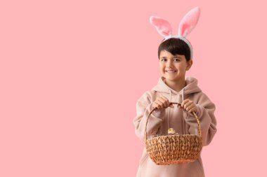 Tavşan kulaklı şirin bir çocuk sepetinde pembe arka planda çikolata yumurtaları tutuyor. Paskalya kutlaması