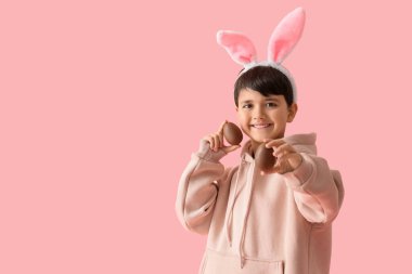 Pembe arka planda çikolatalı yumurtaları olan tavşan kulaklı tatlı bir çocuk. Paskalya kutlaması