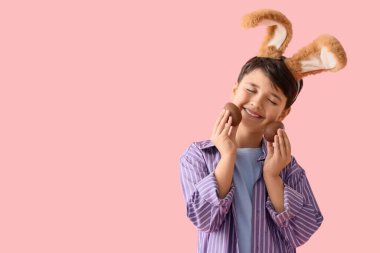 Pembe arka planda çikolatalı yumurtaları olan tavşan kulaklı tatlı bir çocuk. Paskalya kutlaması