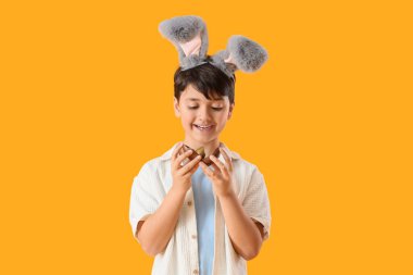 Sarı arka planda çikolata yumurtası olan tavşan kulaklı tatlı bir çocuk. Paskalya kutlaması