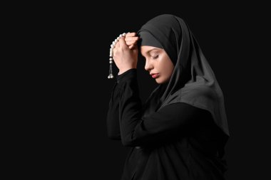 Tasbih 'li genç Müslüman kadın siyah arka planda dua ediyor. Ramazan kutlaması