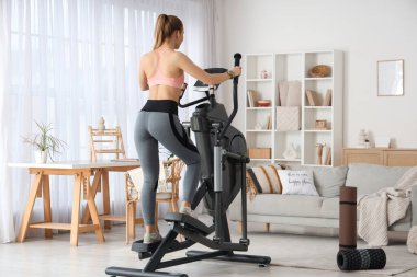 Spor yapan genç bir kadın modern egzersiz bisikleti üzerinde çalışıyor.