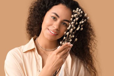 Beautiful young African-American woman with pussy willow branches on brown background