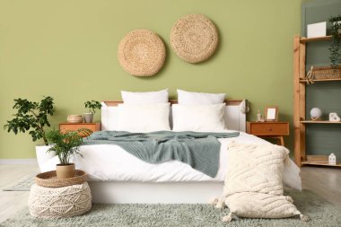 Yatak odasının içinde komodinlerin, ev bitkilerinin, rattan pufların, yastıkların ve yatağın olduğu oda.